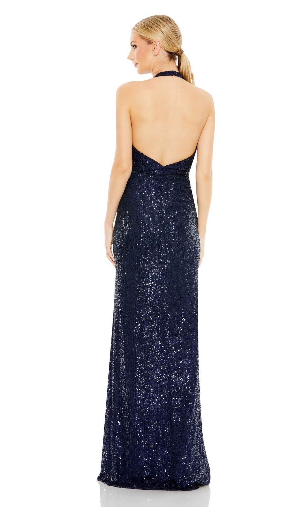 A woman in the Mac Duggal Long Formal Dress 11277, a navy blue sequin halter neck gown with a chic backless design, stands facing away with her hair in a low ponytail, showcasing an elegant silhouette.
